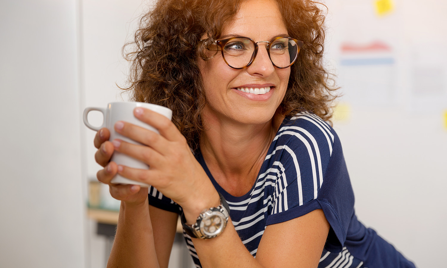 Frau mit Brille und Locken hält Kaffeetasse in der Hand und freut sich über die Unterstützung auf dem Weg zu ihrem Traumjob